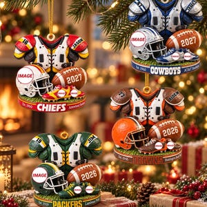 Puede incluir: Cuatro adornos navideños con temática de fútbol americano que incluyen camisetas, cascos, balones y tacos. Cada adorno muestra el nombre del equipo, estadio, año de fundación y detalles del jugador. Los diseños incluyen Chiefs, Cowboys, Browns y Packers.