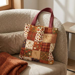 May include: A patchwork tote bag featuring a variety of autumn-themed fabric squares. The design includes patterns of pumpkins, fall leaves, wheat stalks, and plaid prints in shades of orange, brown, green, and cream with two dark red handles.