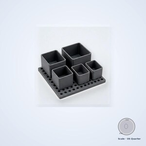 May include: A dark gray modular desk organizer set featuring a square base plate with a grid of circular holes and five removable square containers of varying heights. A US quarter coin is included for scale, measuring 0.955 inches in diameter.