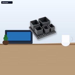 May include: A dark gray desk organizer set featuring a square base with a grid of circular holes and five removable square containers of varying sizes. The organizer is positioned next to a rectangular blue screen and a white mug on a flat surface.