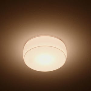 Op de afbeelding: Een ronde plafondlamp met een gladde, ondoorzichtige witte glazen kap die een warm, diffuus licht uitstraalt. Het armatuur heeft een eenvoudig, strak ontwerp met een dunne, neutraal gekleurde rand voor een gelijkmatige verlichting.