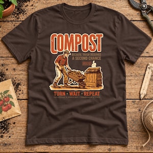 May include: A dark brown t-shirt featuring a graphic of a person pushing a wheelbarrow filled with organic matter toward a wooden compost bin. The text reads COMPOST BECAUSE TRASH DESERVES A SECOND CHANCE, TURN WAIT REPEAT, and YESTERDAY'S PROBLEM TOMORROW'S SOIL.