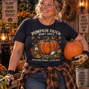 May include: A dark navy blue short-sleeve t-shirt featuring a graphic print of a large orange pumpkin, a lantern, and a garden trowel. The text reads PUMPKIN PATCH NIGHT SHIFT and BACKYARD GROWN AFTER DARK, surrounded by autumn leaves and a crescent moon.