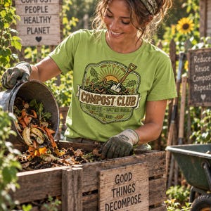 May include: A light green t-shirt featuring a graphic of a shovel, sun, and worms with the text COMPOST CLUB, FEED THE SOIL, GROW THE FUTURE, and EST. 1936. The design is enclosed in a decorative border with wheat stalks and oak leaves.