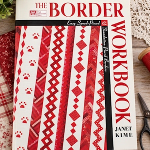 May include: A softcover book titled The Border Workbook by Janet Kime. The white cover features red and white quilt border patterns, including paw prints, diamonds, and zigzags. The text reads The Border Workbook, Easy Speed-Pieced & Foundation-Pieced Borders.