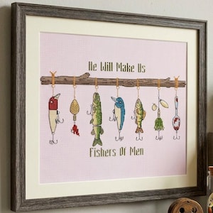 May include: A framed cross-stitch embroidery featuring a horizontal branch with seven colorful fishing lures hanging from it. The text "He Will Make Us" is stitched above the branch, and "Fishers Of Men" is stitched below on a light pink grid.
