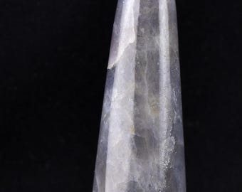 May include: A polished, elongated crystal in shades of blue and gray. The stone has a smooth, glossy surface and a tapered shape, with a rounded base. The crystal is set against a black background, highlighting its natural beauty.