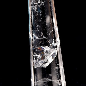 Può includere: Una punta di cristallo di quarzo trasparente con una punta appuntita e una base esagonale. Il cristallo è chiaro e trasparente, con alcune inclusioni interne. Il cristallo è alto circa 15 cm.