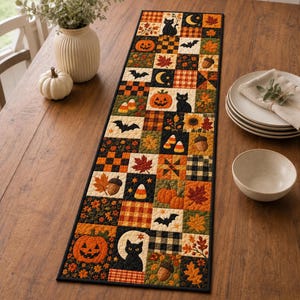 Op de afbeelding: Een rechthoekige gewatteerde tafelloper met een patchworkontwerp van herfst- en Halloween-motieven, waaronder zwarte katten, oranje pompoenen, vleermuizen, eikels, maissnoepjes, zonnebloemen en esdoornbladeren in oranje, zwart en crèmekleur.