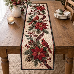 May include: A quilted table runner featuring a cream-colored background with a repeating pattern of red poinsettias, bright red cardinals, green pine branches, brown pinecones, red berries, and a dark red and green plaid ribbon border.