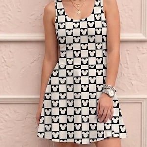 May include: Sleeveless black and white checkered dress featuring a repeating pattern of Mickey Mouse silhouettes. The dress has a scoop neckline and a flared skirt. The model is wearing a watch and necklaces.