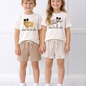 Two children wearing matching white t-shirts with animal designs and the text "Born to be wild" printed on them.