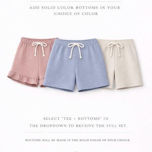 The image is an advertisement for H&G clothing, featuring three pairs of shorts in solid colors - pink, blue, and beige - arranged in a row. The text encourages customers to "Make it a set" by adding solid color bottoms to their choice of color, and provides instructions to "Select 'tee + bottoms' in the dropdown to receive the full set."