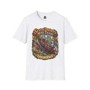 Op de afbeelding: Een wit t-shirt met korte mouwen en een afbeelding van een mijntrein op rails met een waterval en bos. De tekst luidt bovenaan Seven Dwarfs Mine Train en onderaan Heigh-Ho! Off We Go! in een decoratieve bannerstijl.