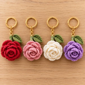 Pode incluir: Quatro porta-chaves de rosas em croché com argolas de metal dourado. Cada porta-chaves apresenta uma flor em vermelho, rosa, branco ou roxo, acompanhada por uma pequena folha verde em croché presa ao caule.