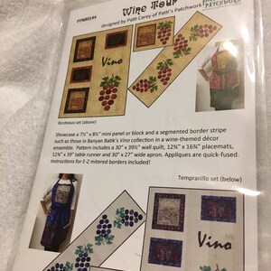 May include: Wine Tour quilt pattern featuring a segmented border stripe with grapes and the word "Vino". The pattern includes instructions for a 30" x 39" wall quilt, 12" x 16" placemats, 12" x 39" table runner, and 30" x 27" wide apron.