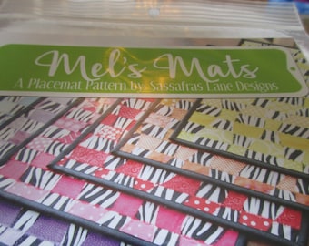 May include: A set of colorful placemats with a zebra print pattern. The placemats are made of fabric and have a black border. The text "Mel's Mats A Placemat Pattern by Sassafras Lane Designs" is printed on the top of the image.