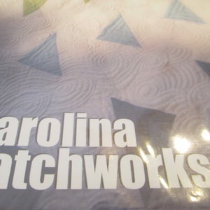May include: Close-up of a white label with the text "carolina patchworks" on a gray and blue patterned background.