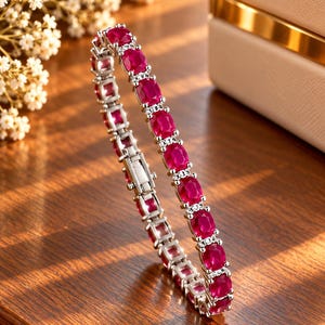 Peut inclure: Un bracelet tennis argenté composé d'une série de rubis rouges vifs de taille ovale. Chaque rubis est serti dans une monture métallique et séparé par de petites pierres d'accent claires et étincelantes, avec un fermoir métallique sécurisé.