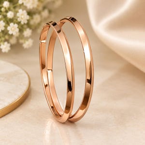 Op de afbeelding: Een paar roségouden oorringen met een gladde, gepolijste afwerking. De oorbellen hebben een cirkelvormig ontwerp met een scharniersluiting en tonen een reflecterend metalen oppervlak dat het licht opvangt voor een strakke uitstraling.
