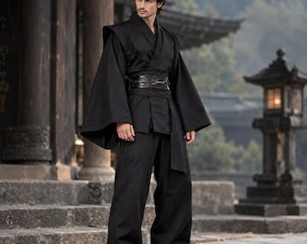 Pode incluir: Um conjunto preto composto por uma parte superior estilo cruzado com mangas largas e fluidas e calças largas a condizer. O conjunto é ajustado na cintura com um cinto preto largo que apresenta um detalhe de fivela metálica.