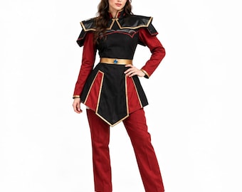 Pode incluir: Um traje composto por uma túnica preta e vermelha com detalhes dourados, ombros estruturados e um cinto dourado com uma gema azul central. O conjunto inclui mangas compridas vermelhas, calças vermelhas a condizer e botins pretos.
