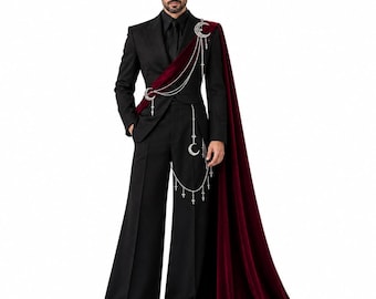 Pode incluir: Um fato preto com calças de perna larga e blazer a combinar, acompanhado por uma capa de veludo bordeaux profundo drapeada sobre um ombro. O conjunto é acentuado por correntes prateadas com pingentes de meia-lua e cruzes.