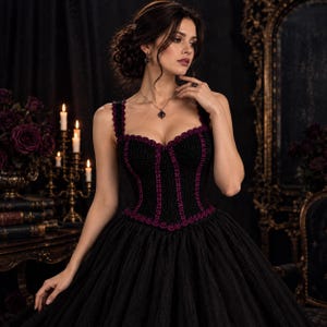 May include: A black corset-style bodice featuring a sweetheart neckline and thick straps, accented with dark purple scalloped trim along the edges and vertical seams, paired with a full-length black skirt with a textured fabric finish.