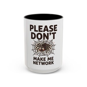 May include: A white ceramic mug with a black interior and rim. The front features a graphic of a small brown spider in a web with the text PLEASE DON'T MAKE ME NETWORK in dark brown, bold, sans-serif capital letters above and below the spider.