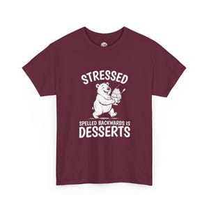 Puede incluir: Una camiseta de manga corta color granate con un gráfico blanco de un oso sonriente que sostiene un gran helado. Sobre el oso aparece el texto STRESSED y debajo el texto SPELLED BACKWARDS IS DESSERTS en letras mayúsculas blancas y negritas.
