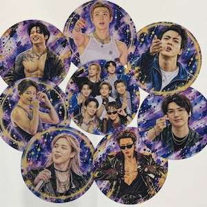 May include: A collection of circular prints featuring portraits of the seven members of the music group BTS. Each circular image displays a member against a vibrant purple and blue galaxy-themed background with gold accents and scattered light dots.