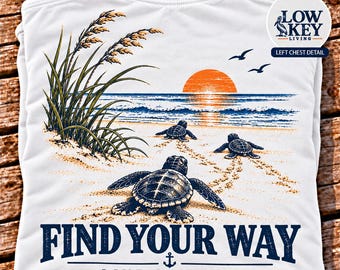 May include: A white t-shirt featuring a graphic of three sea turtles on a sandy beach at sunset, with tall grass, birds, and the text "FIND YOUR WAY" and "LIVE LOW KEY" with an anchor icon. A circular logo reads "LOW KEY LIVING".