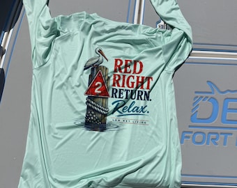 May include: A light mint green long-sleeve shirt featuring a graphic of a pelican perched on a wooden piling with a red triangular sign marked with the number 2. The text reads RED RIGHT RETURN. Relax. LOW KEY LIVING in red and blue.