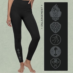 May include: Black high-waisted leggings featuring a vertical row of five grey graphic symbols near the ankle. The symbols include a flaming crest, a Celtic knot shield, a lightning bolt, a dragon key, and a shield with crossed swords and the number 2.