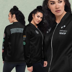 May include: A black bomber jacket featuring a silver front zipper, ribbed collar, and cuffs. The back displays the text SORRENGAIL in grey. The sleeves and chest are adorned with various circular patches and the text SORRENGAIL BWC with wing icons.