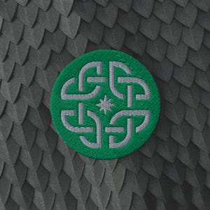 May include: A circular embroidered patch featuring a vibrant green background with a light grey interlaced knotwork design. At the centre of the woven pattern sits a small, eight-pointed star. The patch has a stitched border and a textured finish.