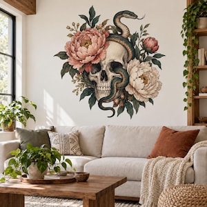 May include: A wall decal featuring a human skull intertwined with a dark green snake, surrounded by large pink and cream-colored peony flowers and green foliage. The design is displayed on a plain white wall above a beige sofa and wooden table.