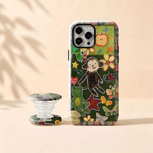 May include: A smartphone case and a matching collapsible phone grip featuring a dark green background with colorful illustrations of a monkey, a frog, butterflies, a ladybug, a red heart with the text I love you, and a red apple.