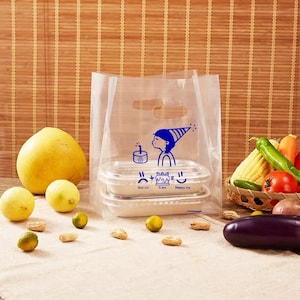 May include: A clear plastic shopping bag with die-cut handles featuring a blue graphic of a person in a party hat and the text "Sad me + Cake = Happy me". Inside the bag are two stacked rectangular food containers with clear lids.