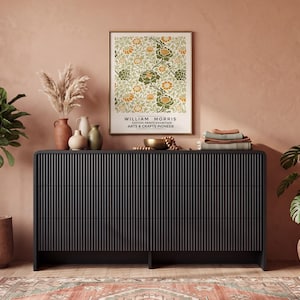 May include: A black rectangular dresser with a vertical ribbed texture across the front, featuring three drawers. Above the dresser hangs a framed poster with a floral pattern and the text William Morris Cotton Prints Exhibition Arts & Crafts Pioneer.