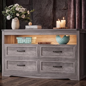 May include: A gray wooden dresser featuring four drawers with black metal handles and an open top shelf illuminated by integrated lighting. The shelf contains a light blue wire basket, a book labeled RUIX, and a textured light blue bowl.