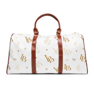 May include: A white duffel bag featuring a repeating gold and tan monogram pattern with the letters LB. The bag includes brown leather-like trim, two top handles, and a zipper closure along the top edge, providing a structured rectangular shape.