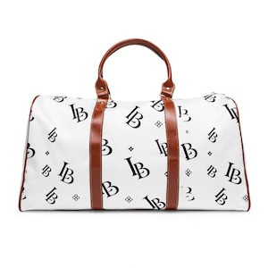 May include: A white duffel bag featuring a repeating black monogram pattern of the letters IB, accented with small four-pointed star symbols. The bag includes two brown leather-like handles and vertical brown trim strips extending down the front.