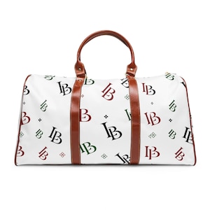 May include: A white duffel bag featuring a repeating pattern of the letters IB in black, dark red, and dark green, accented with small four-leaf clover symbols. The bag includes brown leather-like handles and vertical brown trim accents.