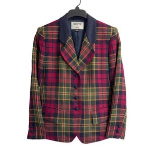 May include: A long-sleeve blazer featuring a red, olive green, and navy blue plaid pattern. The garment has a solid navy blue collar, four navy blue fabric-covered buttons down the front, two front flap pockets, and two buttons on each cuff. The interior label reads KASPER A.S.L.