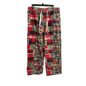 May include: Pants featuring a patchwork design composed of various rectangular fabric segments in red, blue, green, and tan plaid patterns alongside camouflage prints. The garment includes an elastic waistband with a white drawstring cord.