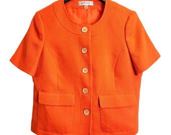 May include: A bright orange short-sleeved jacket featuring a round neckline, five light-colored buttons down the center front, and two rectangular patch pockets at the waist. The interior label displays the brand name Kasper.