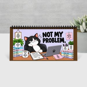 Könnte beinhalten: Ein spiralgebundener Tischkalender mit einer Cartoon-Katze in Schwarz-Weiß, die an einem Schreibtisch mit Laptop sitzt. Der Text lautet NOT MY PROBLEM, Today's Plan und enthält weitere Sprüche auf Büchern und Tassen wie Fueled by not my problem.