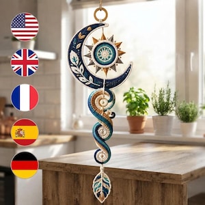 May include: A hanging wall decoration featuring a crescent moon and sun motif crafted with blue, teal, and cream fiber. The design includes a spiraling central column and a leaf-shaped pendant at the bottom, suspended from a circular metal ring.