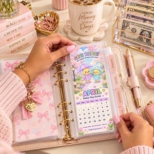 Puede incluir: Un inserto de seguimiento de ahorros para carpeta de anillas con un calendario de abril titulado Rainy-Day Ducks. El diseño incluye dos patitos amarillos bajo paraguas, flores y un arcoíris. El texto dice Save The Day 2027 Kawai Savings Challenge.